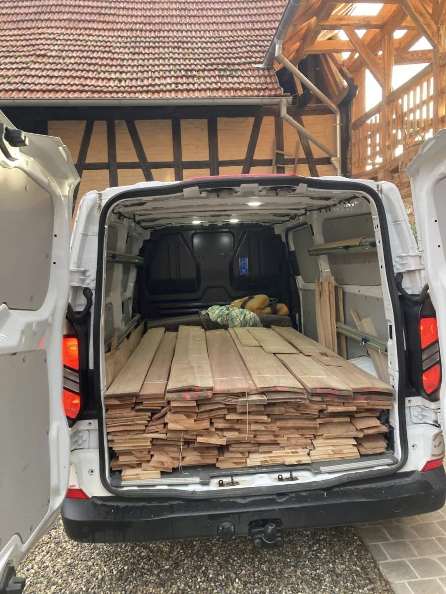 Utilitaire chargé de planches devant un bâtiment à colombages